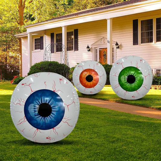 Three bloodshot eyeball Halloween inflatables in blue, orange, and green on a suburban lawn.